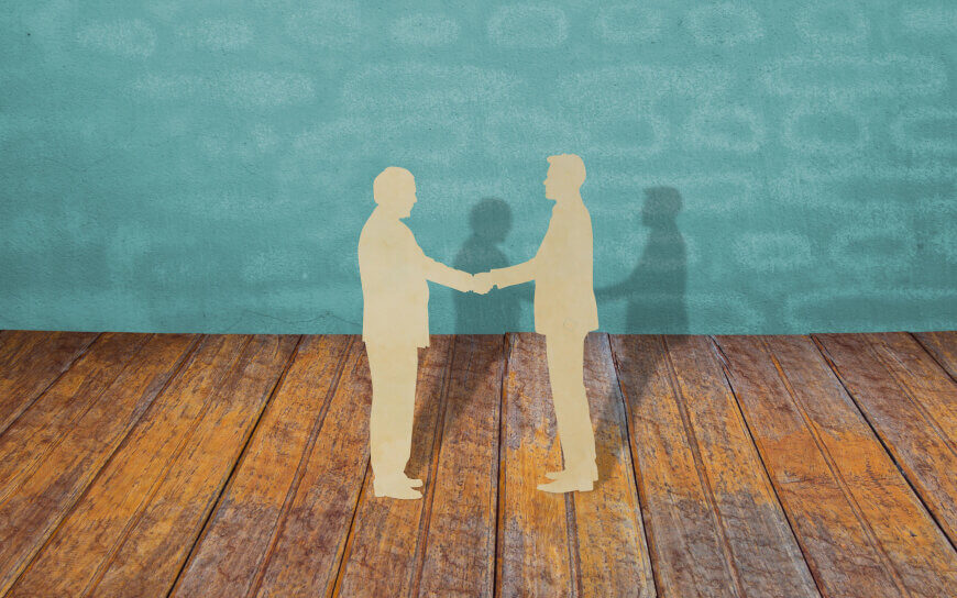 two paper cutouts of business people shaking hands